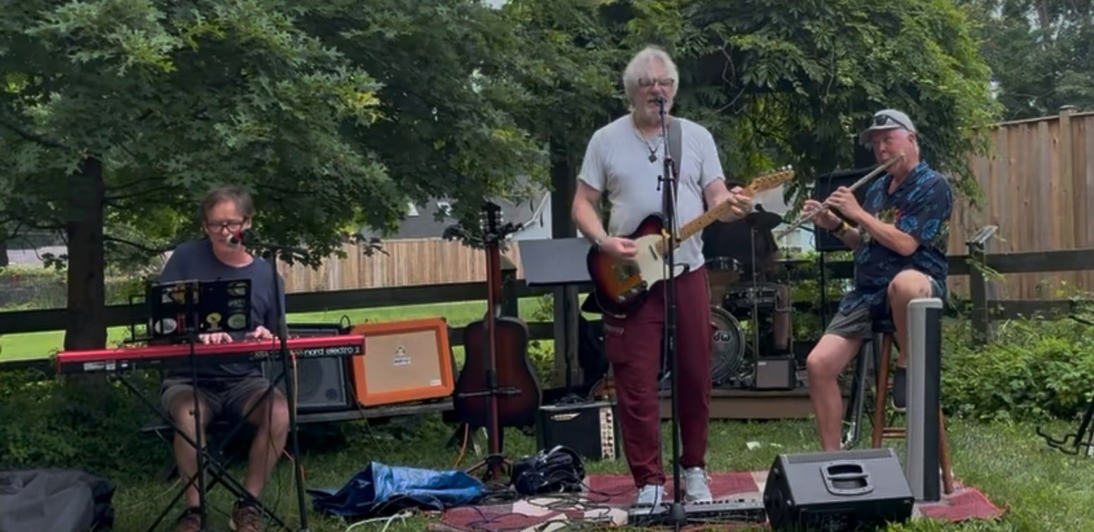 Erich on keys, Frank on guitar and Hunt on flute, playing in a backyard