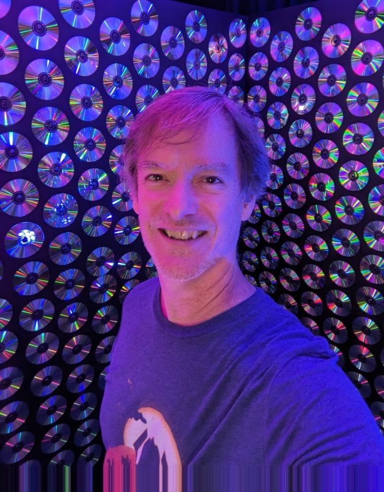 Portrait of Erich Izdepski smiling in front of a wall of CDs